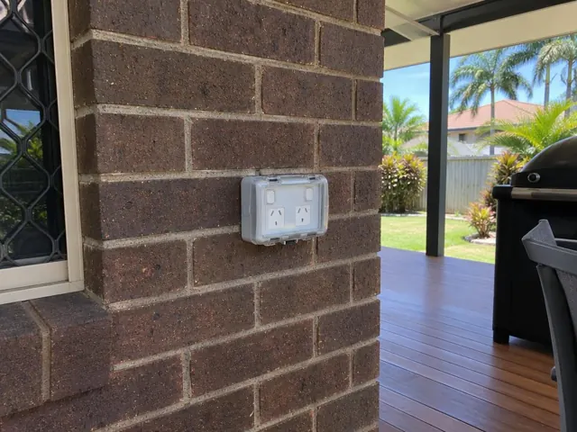 Outdoor double power point with weatherproof cover on a brick patio wall in Runaway Bay