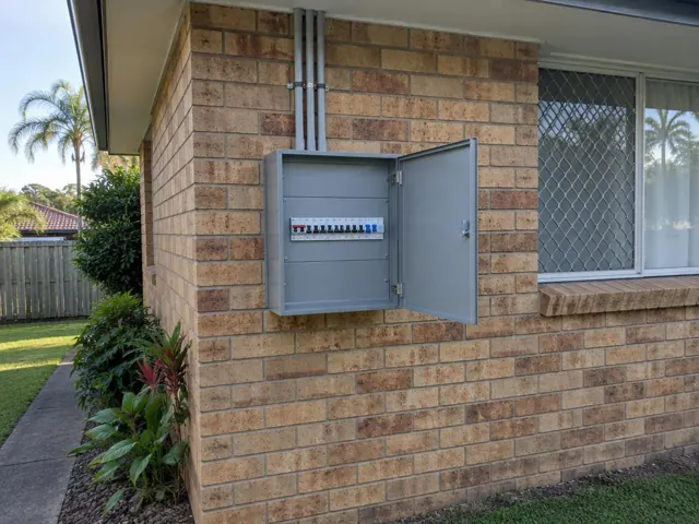 Open external switchboard on a brick house wall beside a window in Coombabah